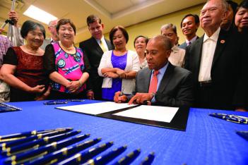 Flanked by advocates including DOT-I's Huong Phan and Mayor Walsh, Gov. Deval Patrick signs the Bilingual Ballot Bill in Chinatown. 